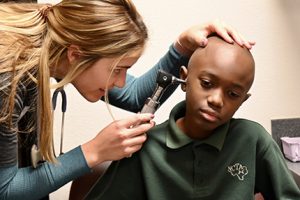 Staff member providing an ear exam for a student.